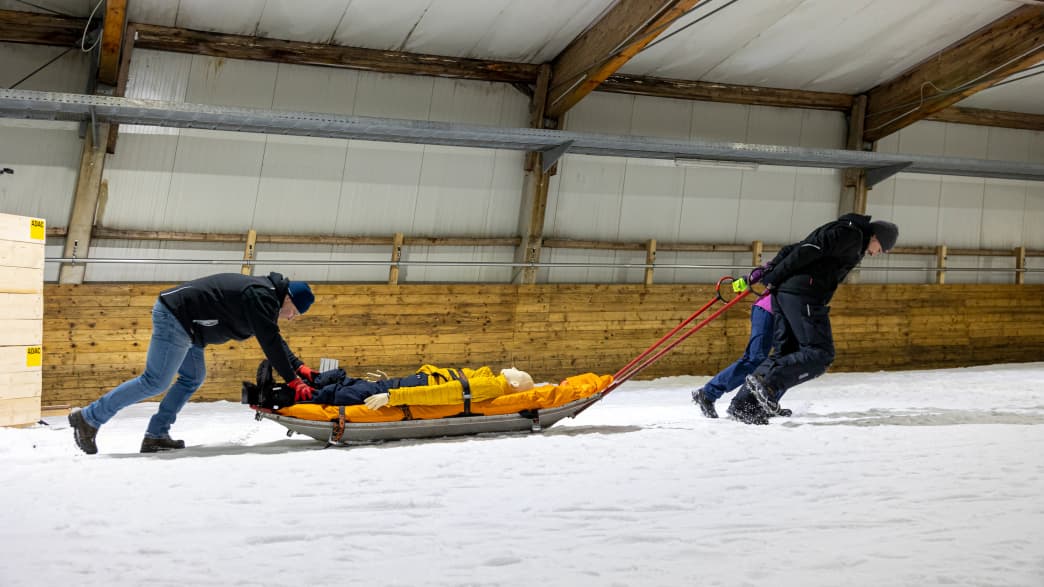 Techniker ziehen einen Dummy eine Piste hoch wärend des ADAC Schlittencrashtest in der Skihalle in Bottrop