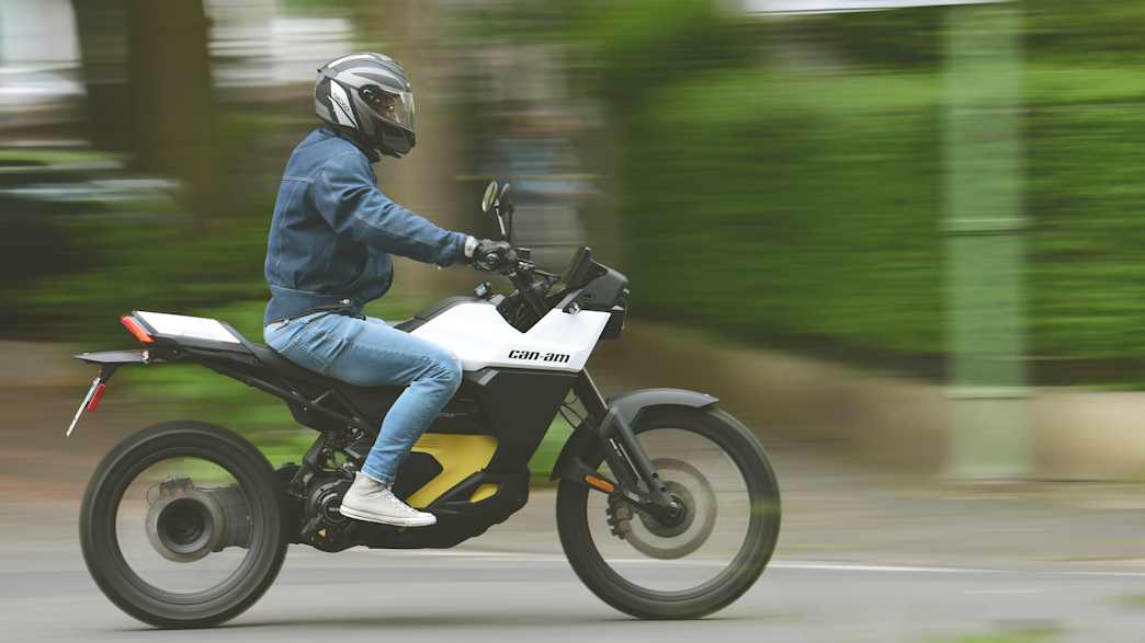 Ein Can Am Origin Elektromotorrad fährt durch eine von grünen Hecken umsäumte Straße