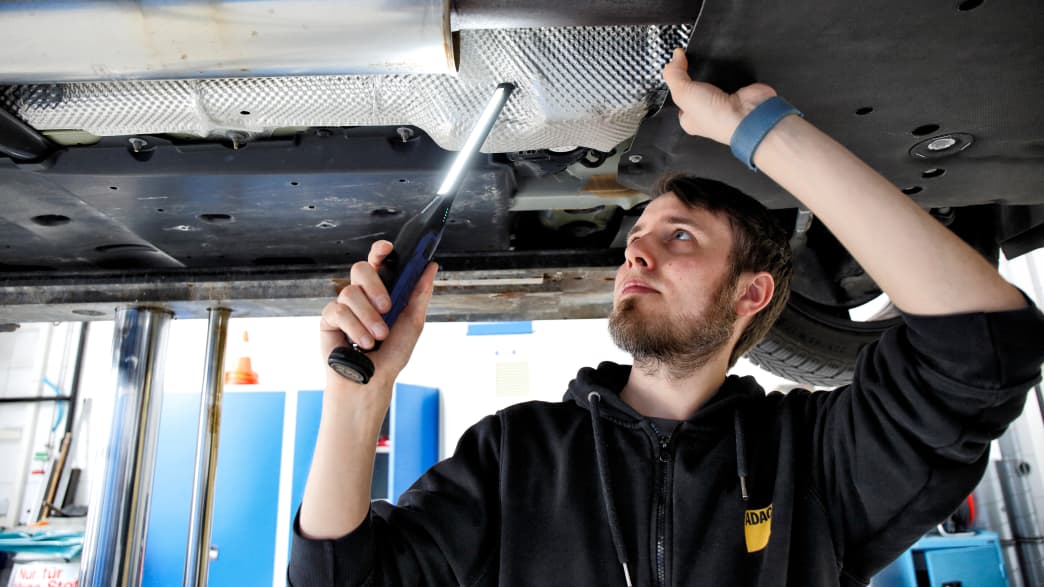 Ein Techniker überprüft den Unterboden eines Autos beim Eco Test 2023 im ADAC Technik Zentrum Landsberg