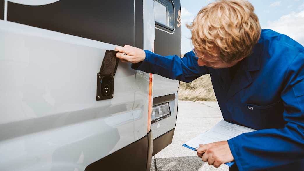 Ein Mann prüft einen Elektrobuchse aussen am Camper