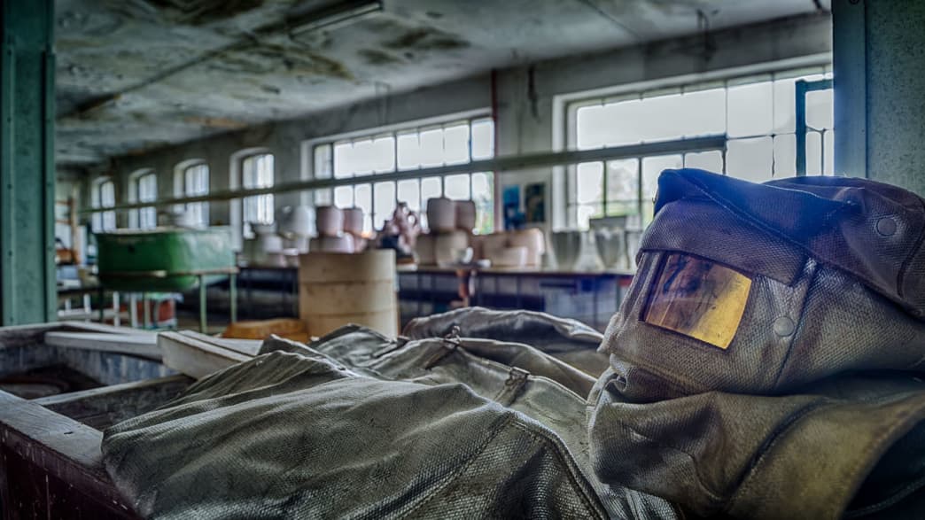 ein Schutzanzug mit Maske liegt am Boden einer verlassenen Porzellanfabrik