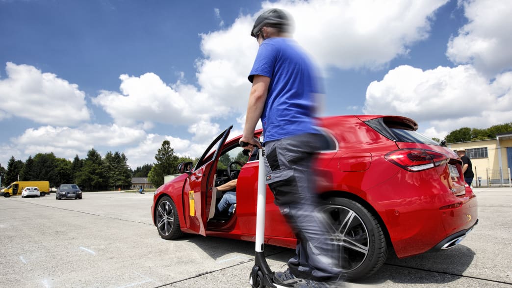 Rollerfahrer fährt an einem roten Auto vorbei, aus dem jemand aussteigt