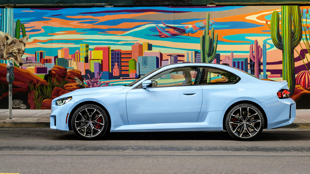 Ein hellblauer BMW M2 parkt vor einem Grafitti