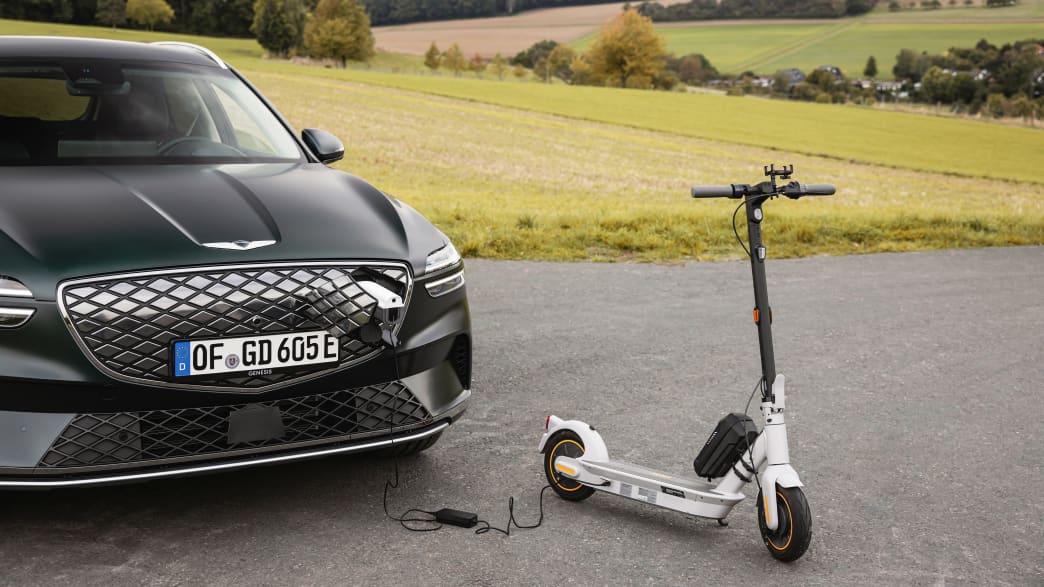 Der Genesis Electrified GV70 und ein Elektroroller stehen in einer Landschaft