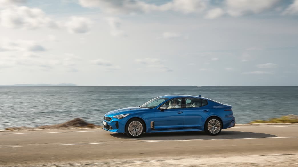 Blauer Kia Stinger 3.3 T-GDI AWD faehrt Kuestenstrasse entlang