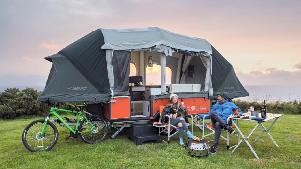 Der Air Opus Zeltanhaenger aufgespannt mit Personen und Fahrrad davor in der Natur