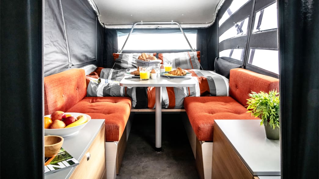 Der Faltcaravan Take Off mit Bett und Bank, Tisch und Frühstück darauf