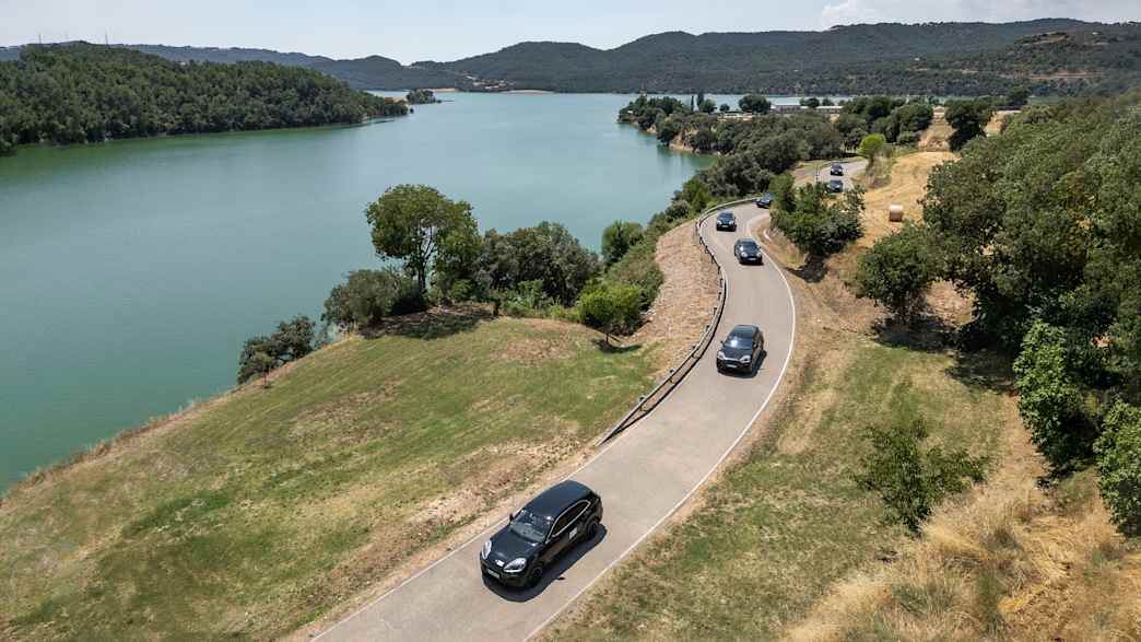 Draufsicht auf vier fahrende Porsche Cayenne E in einer ländlichen Umgebung mit einem See.