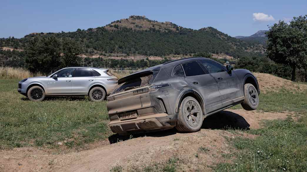 Zwei Porsche Cayenne E fahren über eine steinige Fläche in einer bergigen Landschaft.
