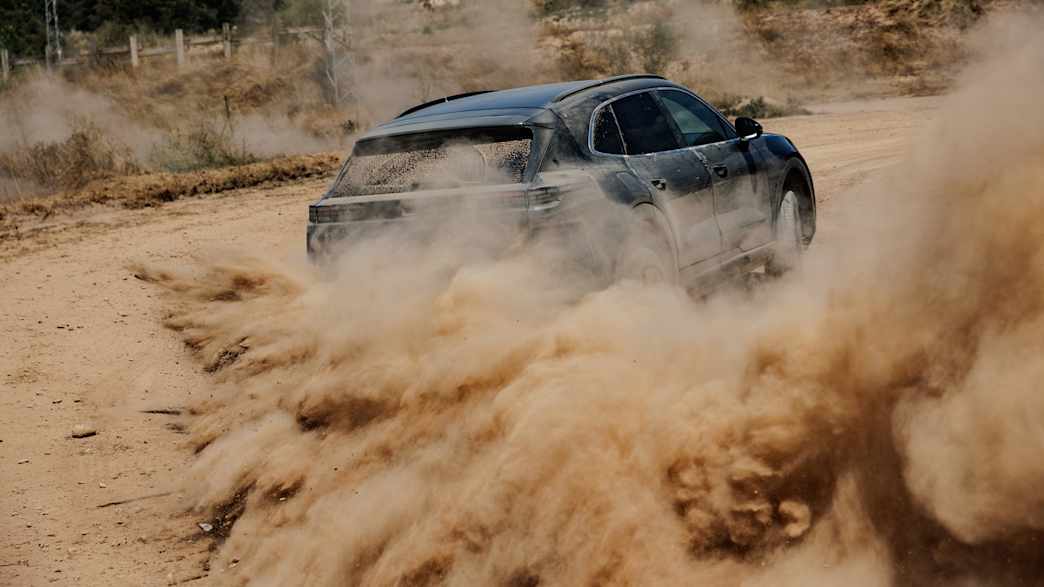 Heckansicht eines fahrenden Porsche Cayenne E der durch eine sandige Umgebung fährt
