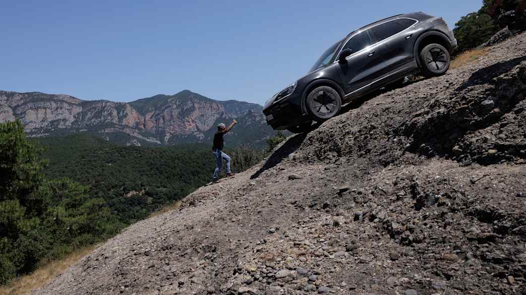 Ein Porsche Cayenne E fährt eine steile Steigung hinab, umgeben von Felsen und Vegetation