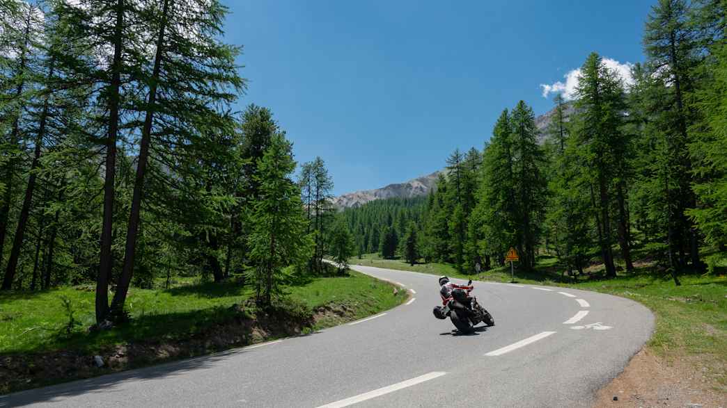 Motorrad auf der berühmten Route des Grandes Alpes mit Blick auf dichte Wälder und hohe Gipfel.