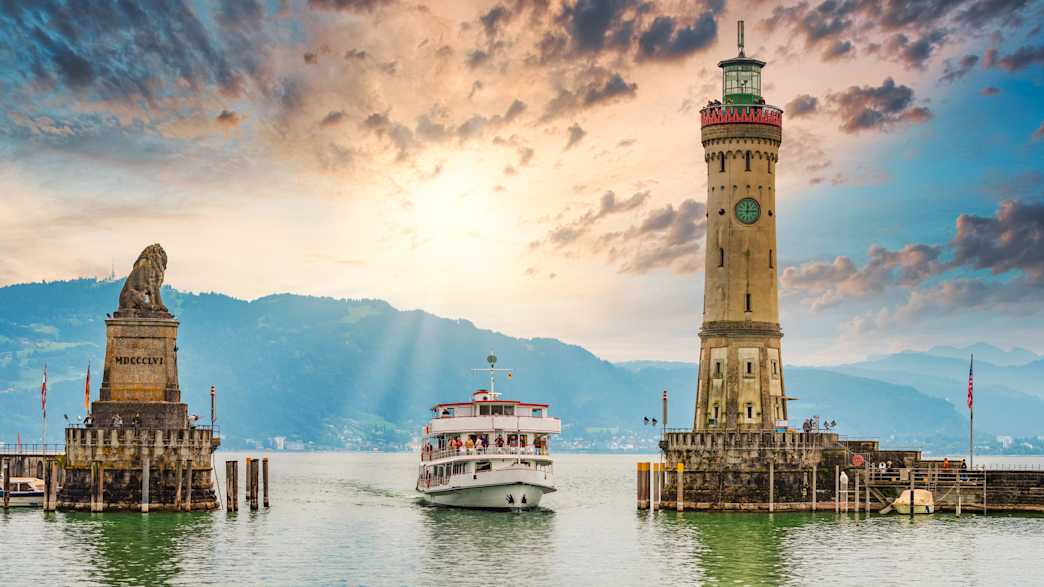 Zwischen der Löwenstatue und dem Leuchtturm am Hafen von Lindau fährt ein Schiff ein