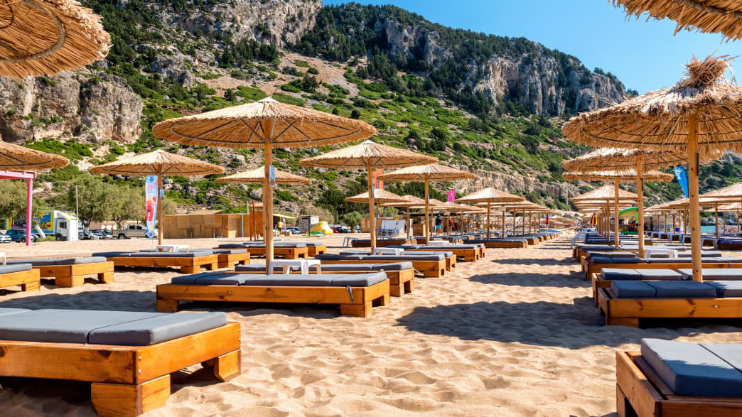 Liegestühle vor einer Felskulisse am Strand von Tsambika, auf der Insel Rhodos