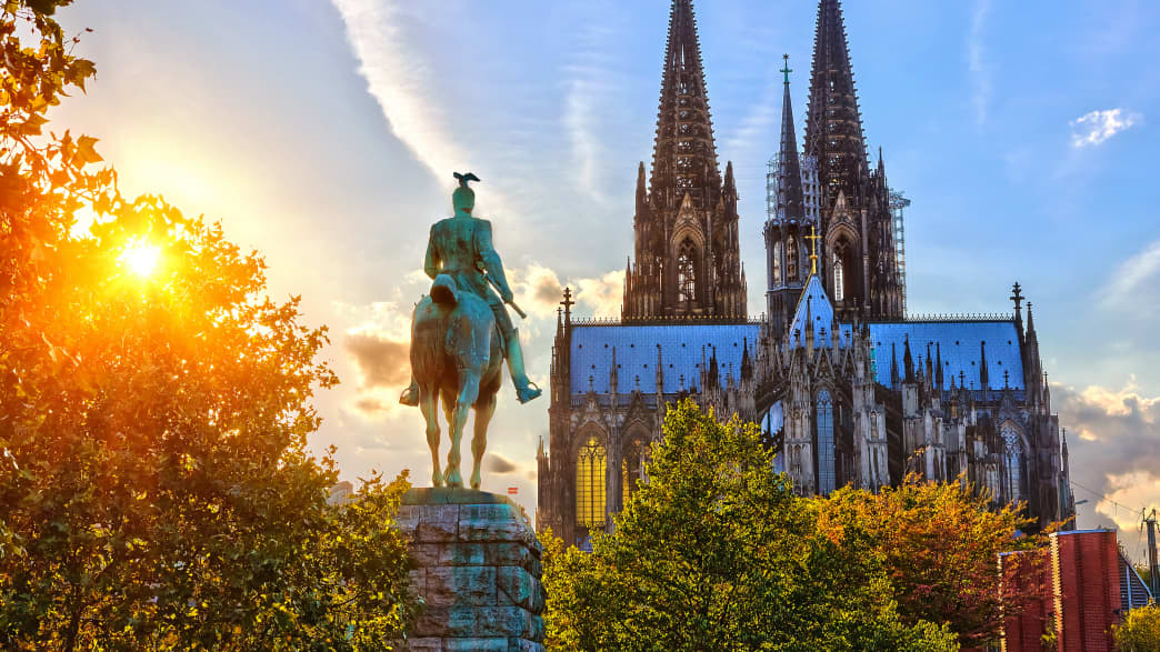 Der Kölner Dom im Sonnenuntergang mit einer Reiterstatue im Vordergrund