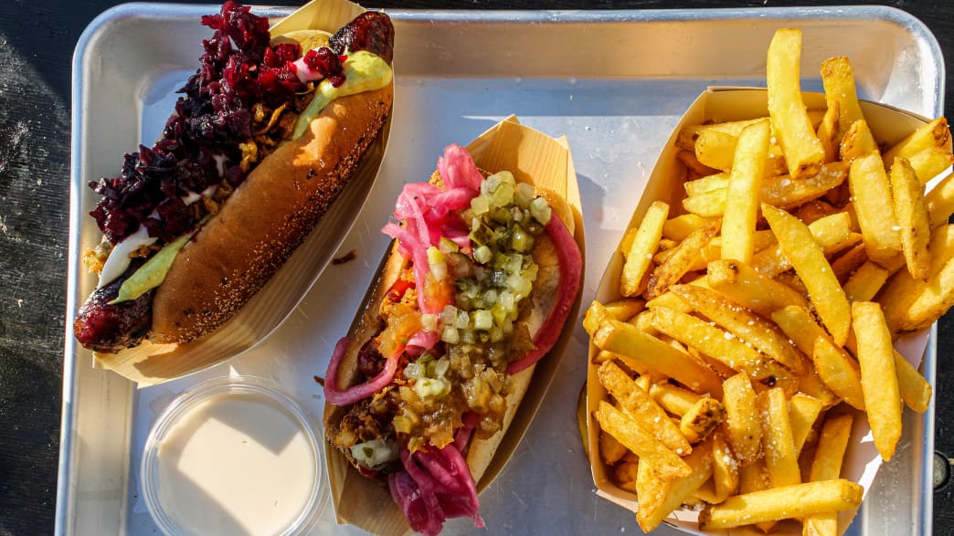 Dänischer Hot Dog mit roter Wurst, garniert mit Remoulade, Ketchup und eingelegten Zwiebeln, serviert in einem Metalltablett.