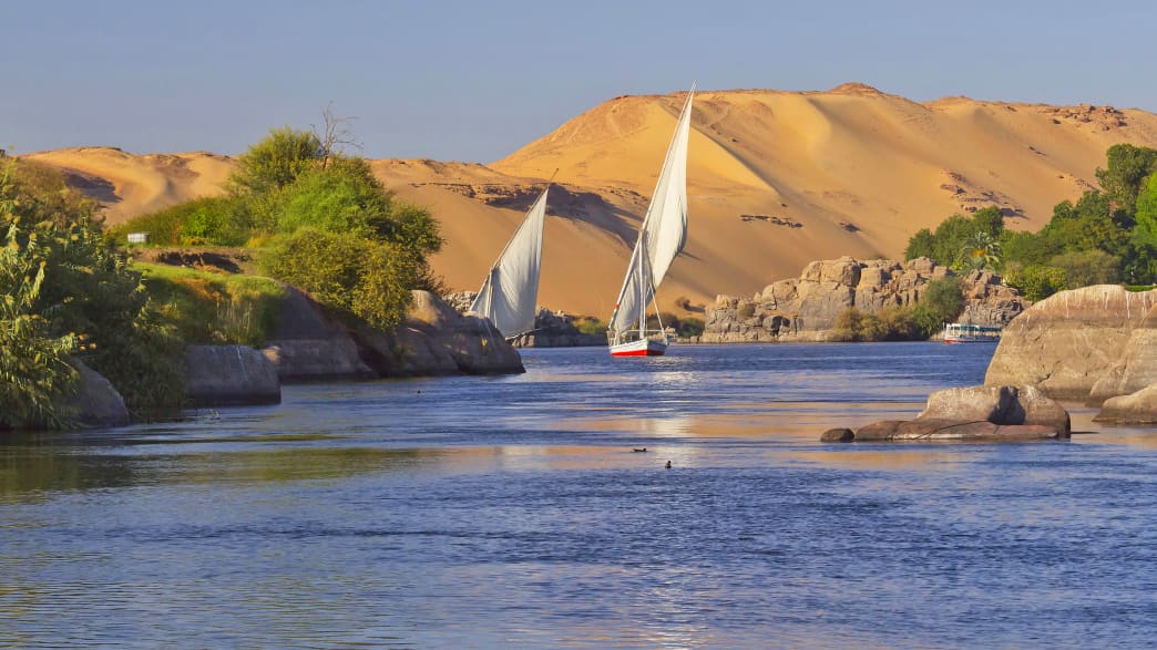 Segelboote auf dem blauen Nil vor Sanddünen bei Aswan, Ägypten