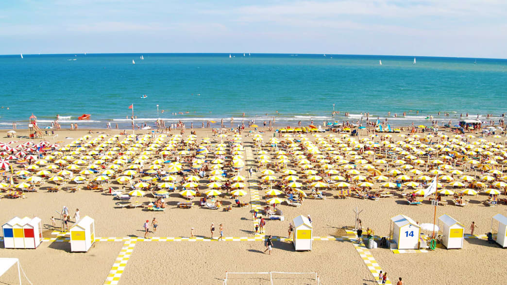 Aufgereihte Sonnenschirme am Sandstrand von Caorle an der italienischen Adriaküste