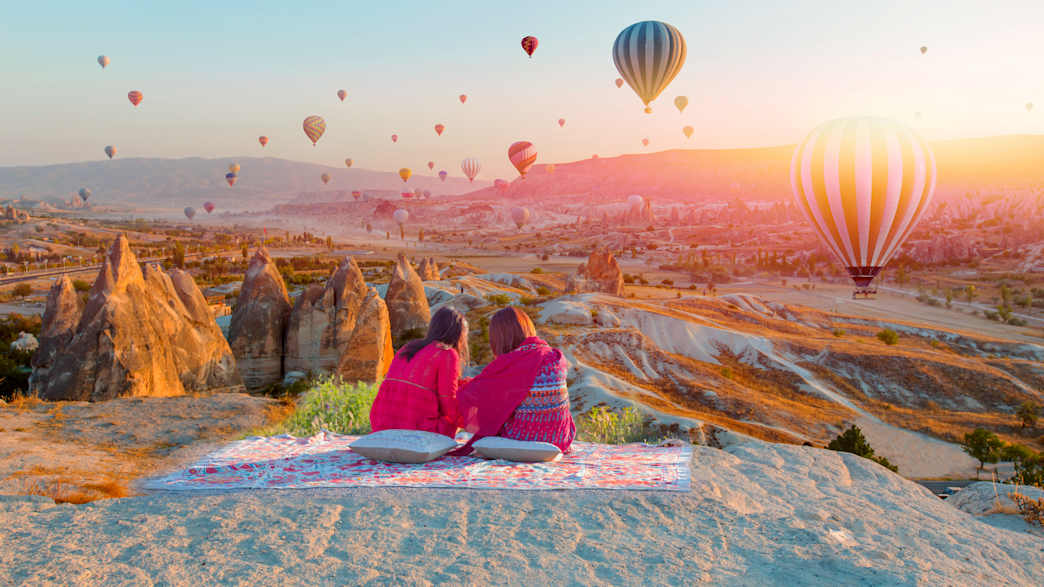 Zwei Mädchen auf einem Hügel beobachten Heißluftballons, die im Abendlicht über Kappadokien fahren