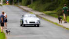 Dieser silberne Porsche verkörpert den klassischen Stil und die sportliche Eleganz der 50er Jahre und fährt durch eine idyllische Dorfstraße.