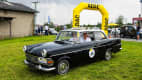 Opel Rekord P2, Baujahr 1962: Ein schwarzer Opel Rekord, der durch das ADAC-Banner fährt, symbolisiert die deutschen Ingenieurskunst und den Charme der frühen 60er Jahre.