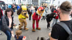 Familienfreundliche Veranstaltung, bei der Menschen mit Maskottchen interagieren, darunter ein Hund in einem gelben Outfit und ein Fuchs in einem roten Anzug.