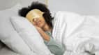 Eine Frau liegt mit einer goldenen Schlafmaske im Bett und schläft.