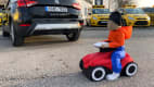 Bobbycar-Dummy fährt hinter einem Auto