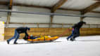 Techniker ziehen einen Dummy eine Piste hoch wärend des ADAC Schlittencrashtest in der Skihalle in Bottrop