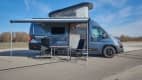 Seitenansicht des Hannes Camper mit aufgebautem Campingset und Dachzelt