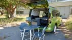 Campingtisch und Stühle hinter dem VW Caddy California Maxi aufgebaut