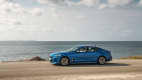 Blauer Kia Stinger 3.3 T-GDI AWD faehrt Kuestenstrasse entlang