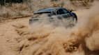 Heckansicht eines fahrenden Porsche Cayenne E der durch eine sandige Umgebung fährt