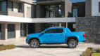 Der neue, blaue Pickup VW Amarok parkend, von der Seite vor einem modernen Wohnhaus