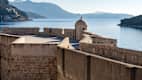 Blick auf die Stadtmauer von Dubrovnik, im Hintergrund blaues Meer und Berge