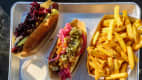Dänischer Hot Dog mit roter Wurst, garniert mit Remoulade, Ketchup und eingelegten Zwiebeln, serviert in einem Metalltablett.