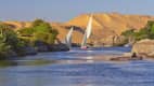 Segelboote auf dem blauen Nil vor Sanddünen bei Aswan, Ägypten