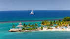 Blick auf einen Sandstrand mit Palmen in Ochio Rios auf Jamaika, im Hintergrund ein Segelboot