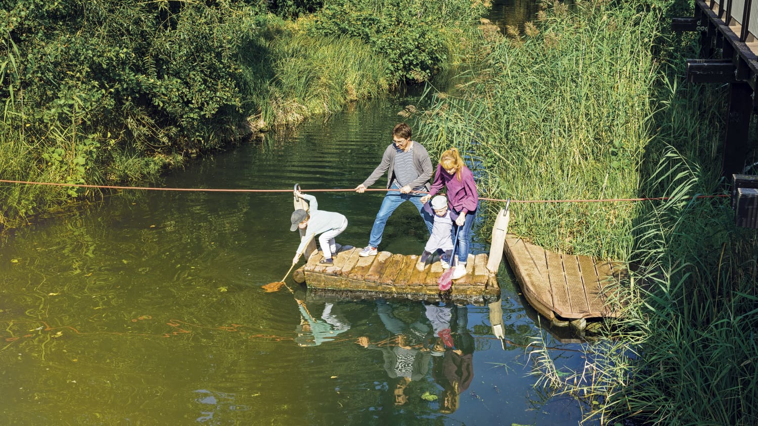 Eine Familie überquert mit einem Floß einen Flusslauf.