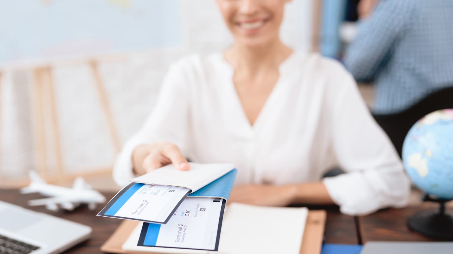 The travel agent keeps tickets for the plane in the travel agency. She offers them to clients. She smiles. On the table she has a toy plane, a laptop.