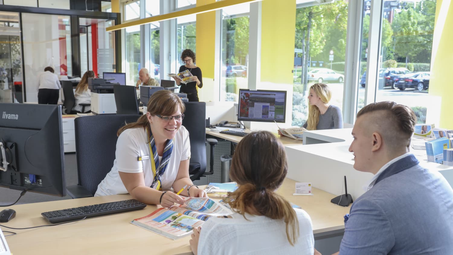 ADAC Mitarbeiterin berät ein junges Paar im Reisebüro.
