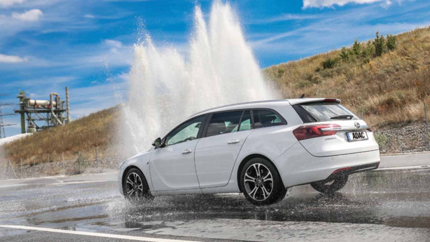 Weißes Auto der Marke Opel fährt bei ADAC Fahrsicherheitstraining durch hochsteigende Wasserfontäne