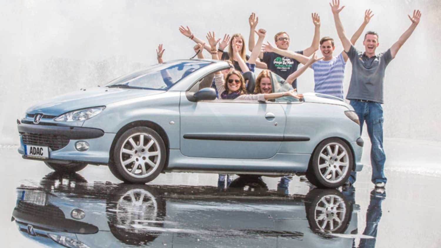 Eine Gruppe junger Menschen steht hinter einem Peugeot und sie strecken jubelnd die Arme in die Luft