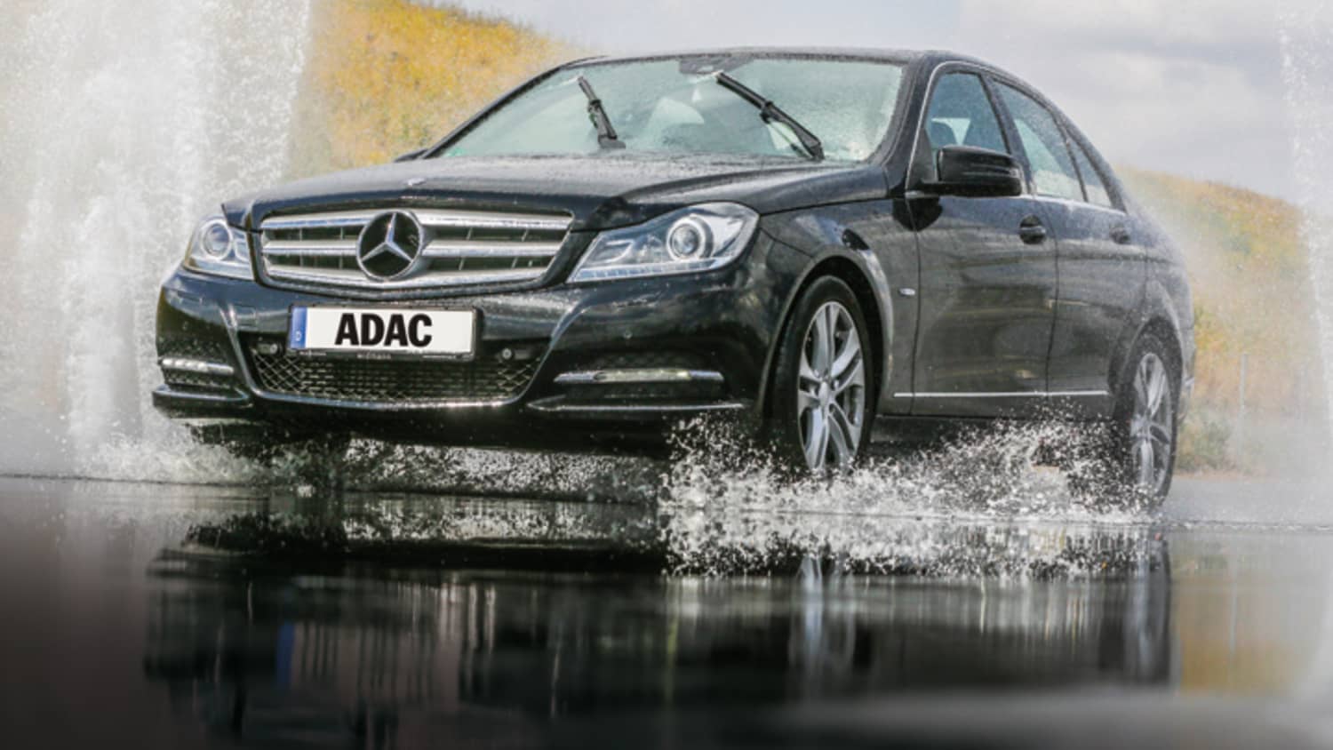 Schwarzer Mercedes fährt auf nasser Fahrbahn und das Wasser spritzt hoch