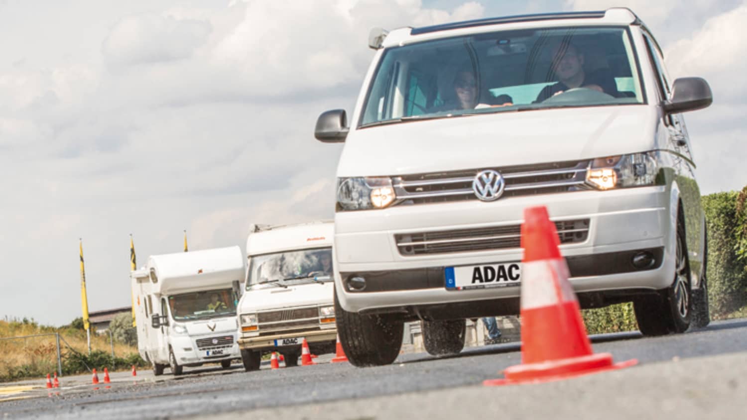 VW Bus und Wohnmobile fahren hintereinander durch einen Slalomparcours