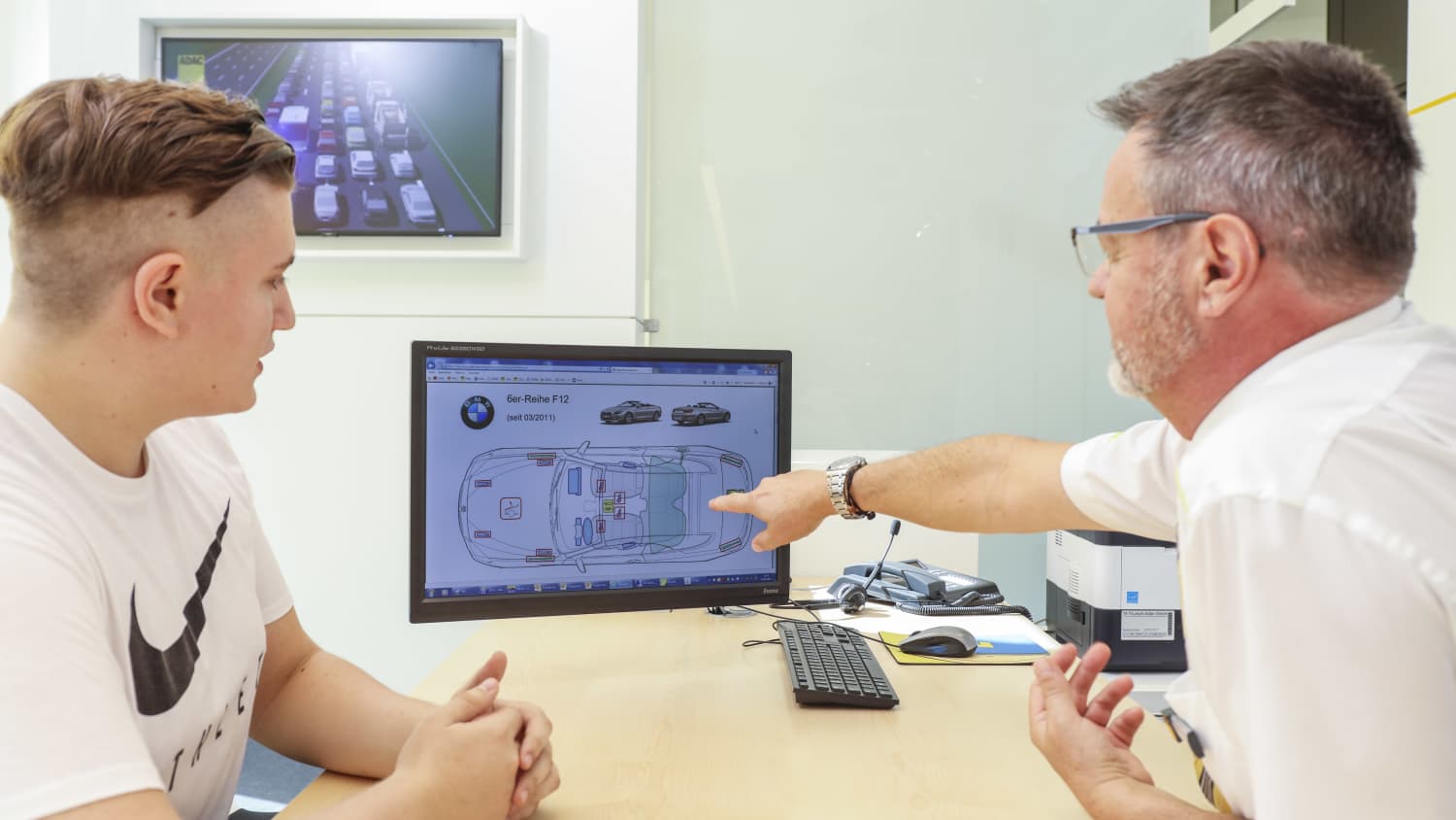 ADAC Verkehrsexperte berät einen Kunden und zeigt ihm am PC die Daten zu einem Auto der Marke BMW