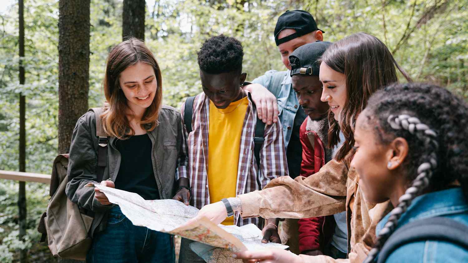 Eine Gruppe an jungen Erwachsenen steht im Wald und schaut auf eine Wegkarte.