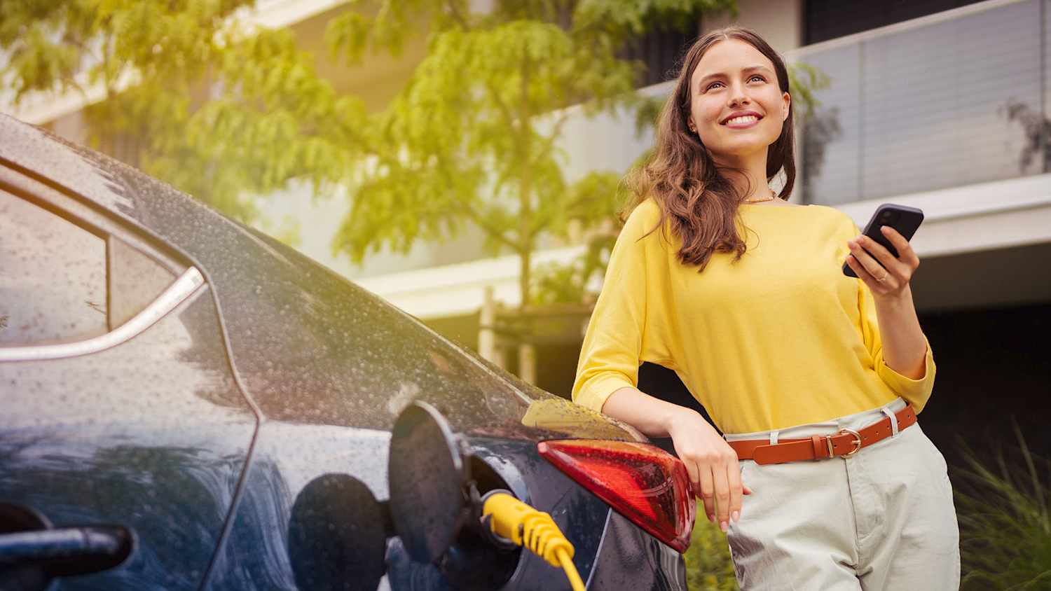 Frau mit Smartphone lädft ein E-Auto
