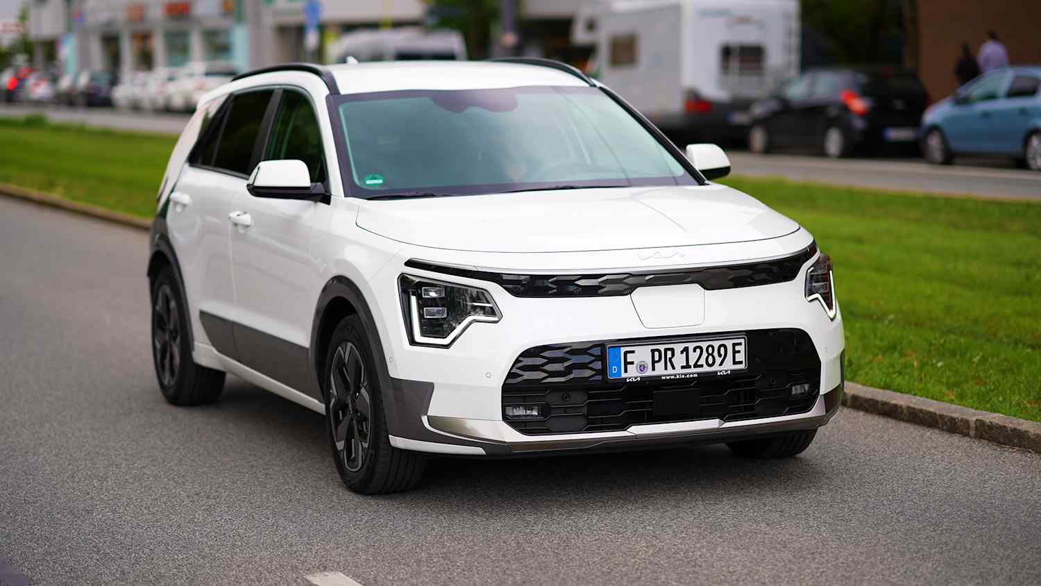 Ein weißer Kia fährt eine Straße entlang und testet die Reichweite des Elektroautos.