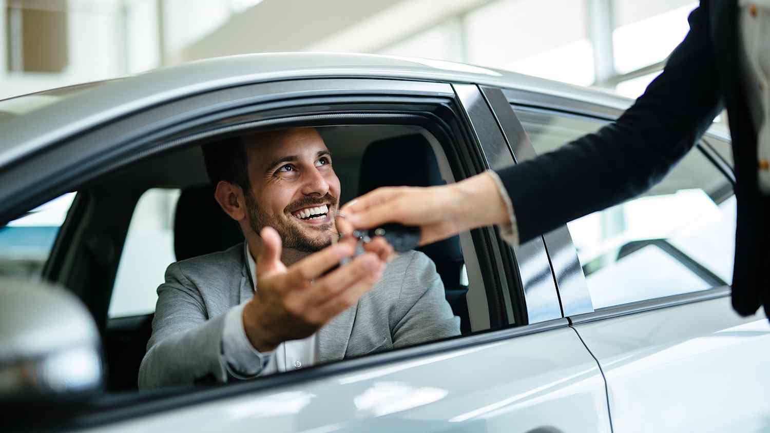 Mann sitzt im neuen Auto und bekommt seinen Autoschlüssel vom Händler